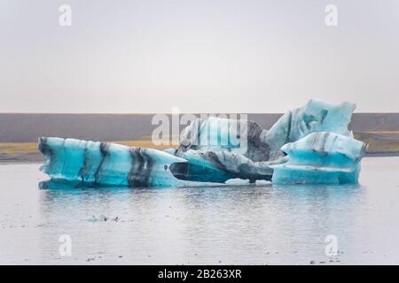 Joekulsarlon Glacier Lagoon tiefblauer Eisberg mit dunklen Schichten vulkanischer Asche, die regelmäßig Muster bilden Stockfoto