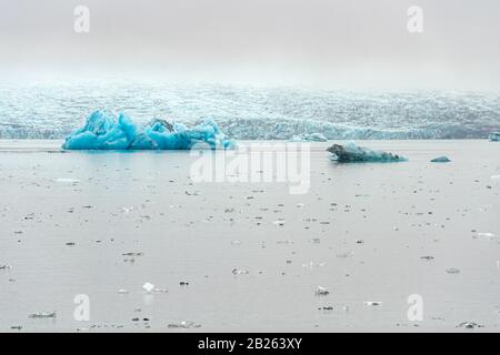 Joekulsarlon Glacier Lagoon tiefblaue Eisberge mit dunklen Schichten vulkanischer Asche groß und klein vor dem Vatnajoekull Gletscher Stockfoto