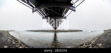 Joekulsarlon Glacier Lagoon Kanal überbrückt durch Hängebrücke, die Eisberge zum Diamond Beach in Island Panorama spült Stockfoto