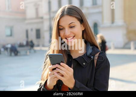 Glückliches Studenten-Mädchen, das Informationen auf dem Smartphone sucht, das in der Straße der Stadt steht Stockfoto