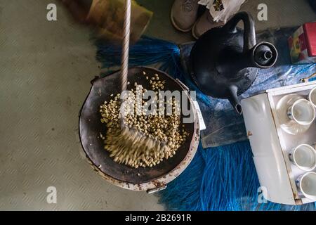 Braten von grünen, unreifen Kaffeebohnen auf einer flachen Pfanne in einem Haus im Süden Äthiopiens Stockfoto