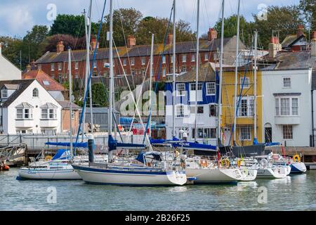 Segelyachten und Boote im Weymouth Harbour mit bunten Häusern an der Jura-Küste von Dorset, South West, Großbritannien Stockfoto