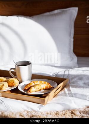 Französische Croissants und schwarzer Kaffee auf dem Tablett im Schlafzimmer zum Frühstück Stockfoto