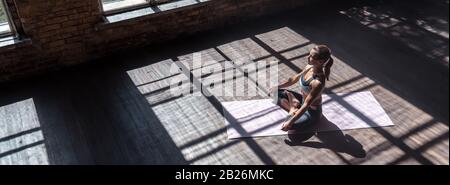 Ruhige Passform gesunde Frau sitzt in lotus-pose und macht Yoga in der Sporthalle, Draufsicht. Stockfoto