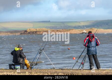 Appletore, Großbritannien. Sonntag, 1. März 2020. Wetter in Großbritannien. Mit Sonnenschein und Schauern, die in Nord-Devon prognostiziert werden, unterhalten sich zwei Angler, während sie vom Kai in Appedore an der Fluss-Torridge-Flussmünde angeln. Kredit: Terry Mathews/Alamy Live News Stockfoto