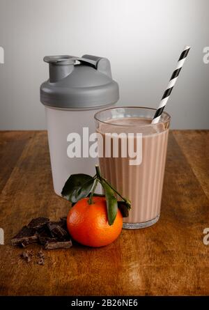 Schokoladenorange Milchshake, Zutaten und Schüttler mit Papierstroh auf einem Holzarbeitspapier Stockfoto