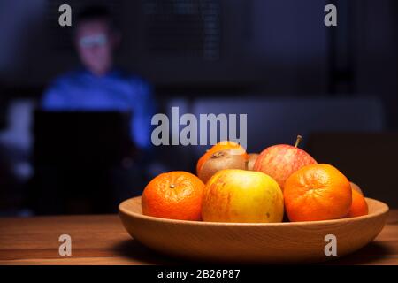 Obstschale auf einem Tisch und Mann, der mit Laptop im Hintergrund arbeitet Stockfoto