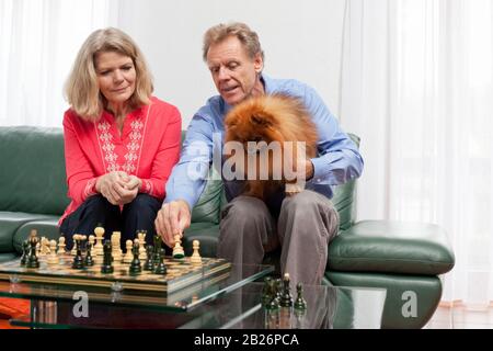 Reifes lächelndes Paar, das in einem hellen Wohnzimmer Schach spielt Stockfoto