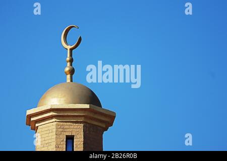 Messing- oder goldfarbenes muslimisches Halbmondsymbol auf der Goldkuppel oben auf dem Minarett der Moschee Stockfoto