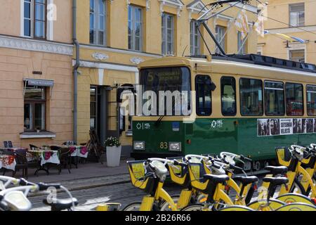 Öffentliche Verkehrsmittel in Helsinki, Finnland: Gelbe Fahrräder gegen eine Straßenbahn auf einer Straße der finnischen Hauptstadt zu mieten Stockfoto