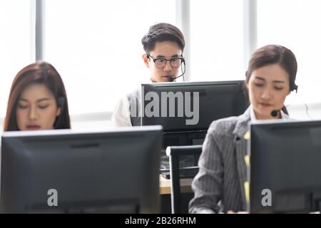 Junge, Erwachsene, freundliche und vertrauensvoll arbeitende Telefonistin mit Headsets, die in einem Callcenter mit ihrem Kollegen arbeiten. Stockfoto