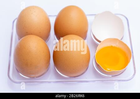 Vier braune Eier lagen auf einem Eiertablett mit einer Eggschale auf weißem Grund. Es gab ein zerbrochenes Ei, das das Eigelb im Inneren zeigte. Stockfoto