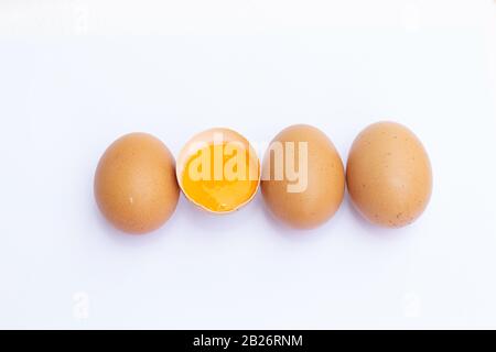 Vier braune Eier, die in einer Reihe auf weißem Hintergrund angeordnet Waren Und ein Ei zur Hälfte gebrochen war, und sahen das Eigelb darin. Stockfoto