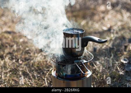 Kaffee auf einem tragbaren Holzbrenner auf dem Zeltplatz in den Bergen zubereiten Stockfoto
