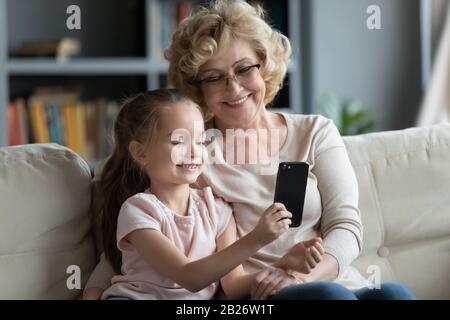 Lächelnde Seniorengrande und kleine Enkelin machen selfie am Telefon Stockfoto