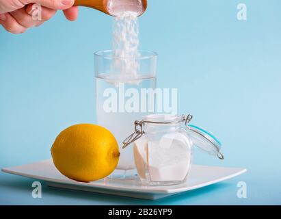 Handgießen von Backsoda im Trinkglas mit Wasser und Zitronensaft, gesundheitliche Vorteile für das Verdauungskonzept. Blauer Hintergrund, Kopierbereich. Stockfoto