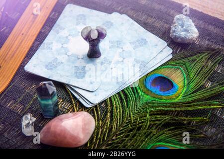 Deck mit selbstgemachten Engelskarten aus Divination auf schwarzem Tisch, umgeben mit Halbedelsteinkristallen. Selektiver Fokus auf Amethys Kristallengel. Stockfoto