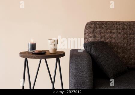 Detailansicht des modernen Couchtisches aus reinem Holz mit Cappuccino-Becher, Glaskerze, die seitlich am Sofa brennt. Stockfoto