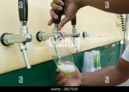 Barkeeper gießt aus frisch gebaschenem Bier in den Plastikbecher. Hände von Barkeeper, die Bierglas aus einem Barkeeper füllen. Hand des Barkeeders, der einen pilsen b gießt Stockfoto