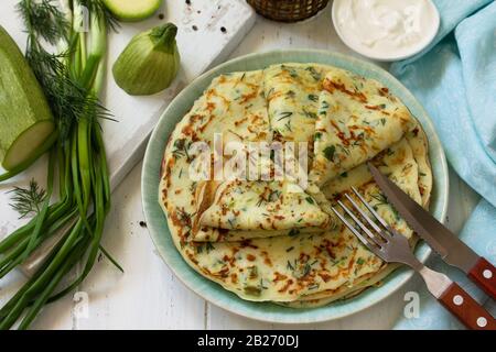 Snack oder Mittagessen im Sommer. Zucchini Pfannkuchen mit Grüns serviert mit saurer Sahne auf einem Holztisch. Stockfoto