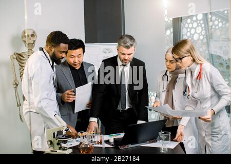 Multiethnische Gruppen von Geschäftsleuten, Ärzten und Wissenschaftlern treffen sich, kooperieren und diskutieren über neue Projekte, klinische Studien oder wissenschaftliche Forschung. Stockfoto