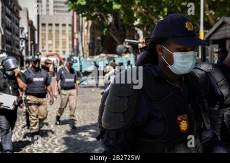 Ein südafrikanisches Polizeimitglied donnt beim Ausbruch des Coronavirus während der Räumung ausländischer Staatsangehöriger vom Kapstädter Greenmarket Square eine Maske Stockfoto