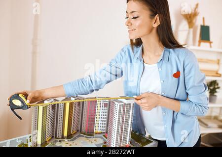 Junge, fleißige Frau hat das Baumodell hergestellt und sie misst es im Architektenstudio, Nahaufnahme Stockfoto