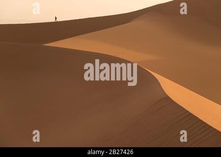 Sanddünen nah und eine kleine Wander-Silhouette im Hintergrund. Stockfoto