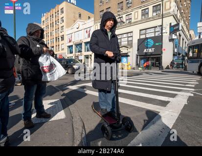 Ein chinesischer Amerikaner mittleren Alters auf einem elektrischen Roller wartet darauf, dass die Ampel auf Main St. in Chinatown, Flushing, Queens, NYC umsteigt Stockfoto