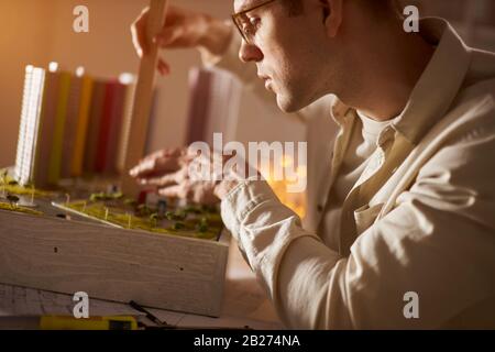 Junger cleverer Mann in Brille, der im Büro auf dem Tisch arbeitet und die Waage eines Massenmodells misst, Nahaufnahme des Seitenbildes Stockfoto