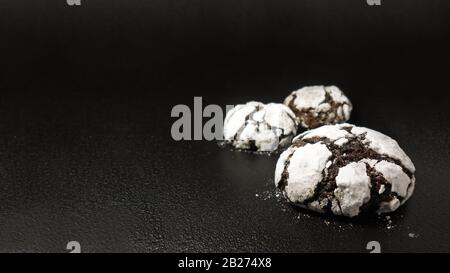 Hausgemachte Schokoladenplätzchen. Schokoladen-Brownie-Plätzchen in Puderzuckerpulver im schwarzen Hintergrund. Selektiver Fokus Stockfoto
