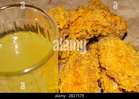 Panierte Hühnerflügel und ein Glas Limonade auf grauem Papierhintergrund. Nahaufnahme Stockfoto