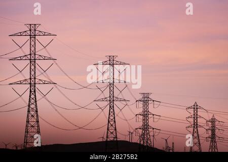 Blick auf den Sonnenuntergang über Hochspannungstürmen auf den Hügeln der Bucht von San Francisco; Windturbinen im Hintergrund; Kalifornien Stockfoto