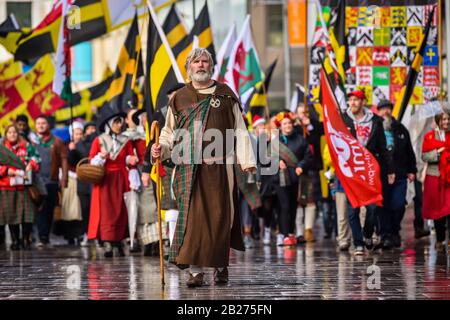 Ein Mann, der als Dewi Sant verkleidet ist, führt die St David's Day Parade in Cardiff an, wo Hunderte von Menschen in der Feier des Schutzpatrons von Wales, Dewi Sant (Saint David in English), der walisischer Bischof von Mynyw (heute St Davids) im 6. Jahrhundert war, durch die Stadt marschieren. Stockfoto