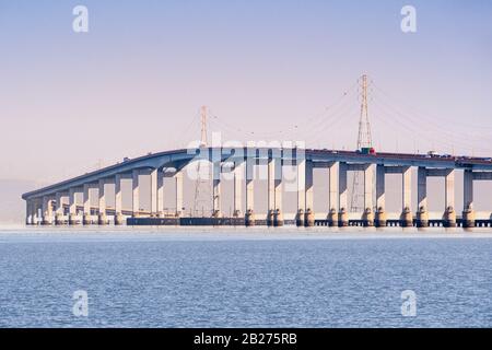 San Mateo Bridge verbindet die Halbinsel und die East Bay in San Francisco Bay Area, Kalifornien; Stromtürme und Stromleitungen sind dahinter sichtbar Stockfoto