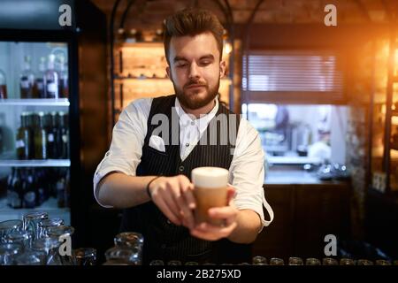 Der junge talentierte und attraktive Barista hat leckere Latte, Nahaufnahmen gemacht. Servicekonzept, Beruf, Beruf und Beruf. Der Mensch bedient Kunden in Stockfoto