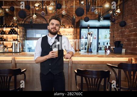 Der junge, freundliche, gut aussehende Mann bedient Kunden in einem Café, Nahaufnahme Foto. Business.Guy arbeitet in einem Kaffeehaus Stockfoto