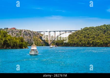 Touristenboote im Krka National Park, Kroatien. Sibenik-Brücke über den Fluss Krka mit klarem Wasser und blauem Himmel an einem sonnigen Tag. Stockfoto