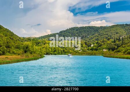 Grüne Hügel mit Wald rund um den Fluss Krka im wunderschönen Nationalpark Krka, Kroatien. Touristische Boote fahren auf dem Fluss entlang, um Skradinski buk waterfal anzukommen Stockfoto