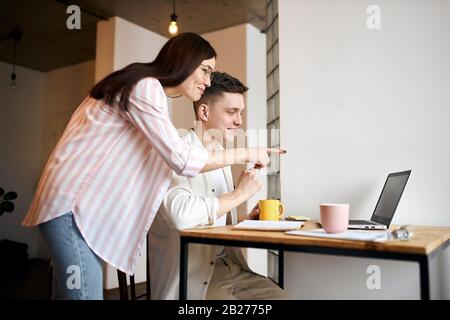Fröhliche liebende Leute, die Videoanruf tätigen, ein Haus wählen, Möbel bewohnen, Fotos mit Seitenansicht aus der Nähe anzeigen Stockfoto