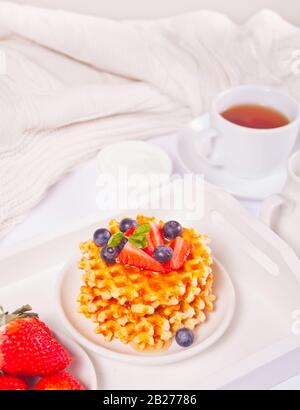 Teller mit süßen, leckeren Waffeln mit Honig, Beeren und einer Tasse Tee auf weißem Hintergrund Stockfoto