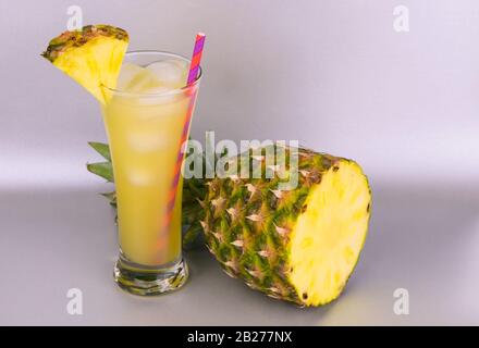 Ananasaft in einem hohen Glas und Ananas auf grauem Hintergrund. Kopierbereich. Stockfoto