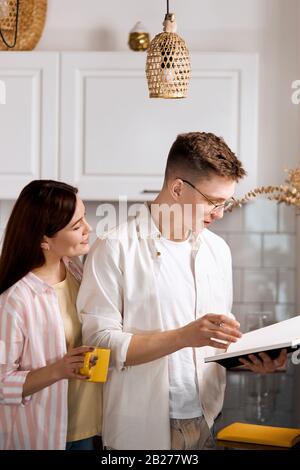 Talentierter Schriftsteller, der sein Spiel vor Frau liest, während er in der Küche steht. Nahaufnahme der Seitenansicht. Vertikaler Schuss. Stockfoto