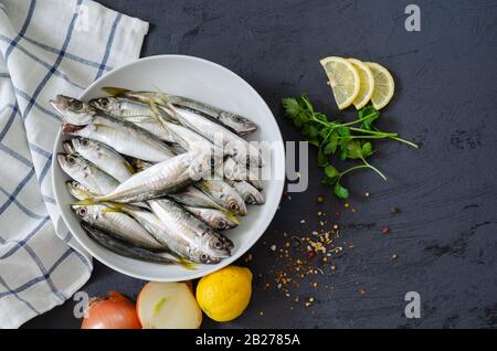 Köstlicher frischer Fisch, aromatische Kräuter, Gewürze und Zitrone auf schwarzem Grund. Mediterrane Küche. Draufsicht. Gesundes und diäumtes Lebensmittelkonzept. Rohdaten Stockfoto