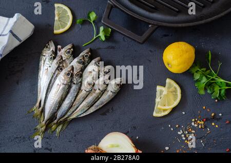 Köstlicher frischer Fisch, aromatische Kräuter, Gewürze und Zitrone auf schwarzem Grund. Mediterrane Küche. Draufsicht. Gesundes und diäumtes Lebensmittelkonzept. Rohdaten Stockfoto