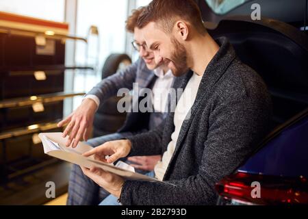 Positiv lächelnder Shop-Assistent und Kunde füllen die Dokumente bei Motorschau aus, Nahansicht Foto. Papierarbeit, Händlerberatung bei einem Kunden, t Stockfoto