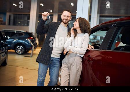 Liebevoll fröhliches Paar holt sich neues Auto aus Loterry. Nahaufnahme Foto, rote und blaue Autos im Hintergrund des Fotos Stockfoto