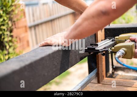 Nahaufnahme eines Tischlers mit einem Luftnagelgewehr, um Holztisch im Garten zu vervollständigen Stockfoto