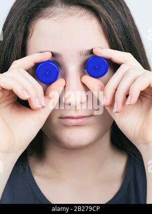 Porträt eines Brunette Teen Girl mit Blue Plastic Bottle Caps Closeup Stockfoto