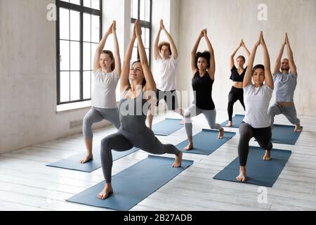 Verschiedene Leute praktizieren Asana mit Trainer, der Warrior One Asana macht Stockfoto